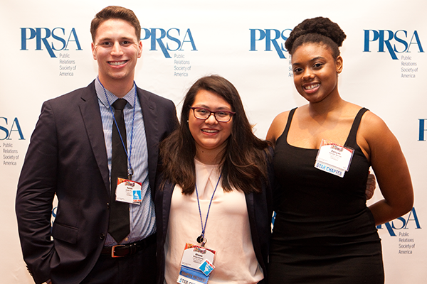 Three PRSA members smiling at the camera standing infront of a PRSA step-and-repeat. They are dressed in business and formal attire.